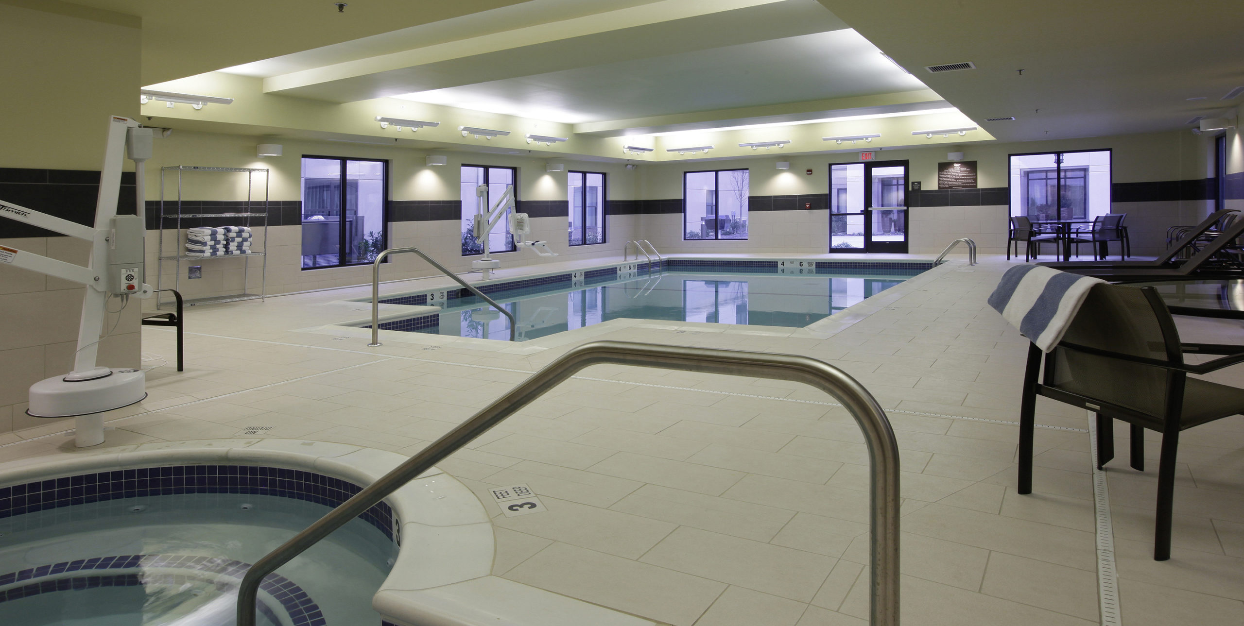 Indoor pool deck with lounge chairs at Homewood Suites by Hilton Carle Place in Garden City, NY