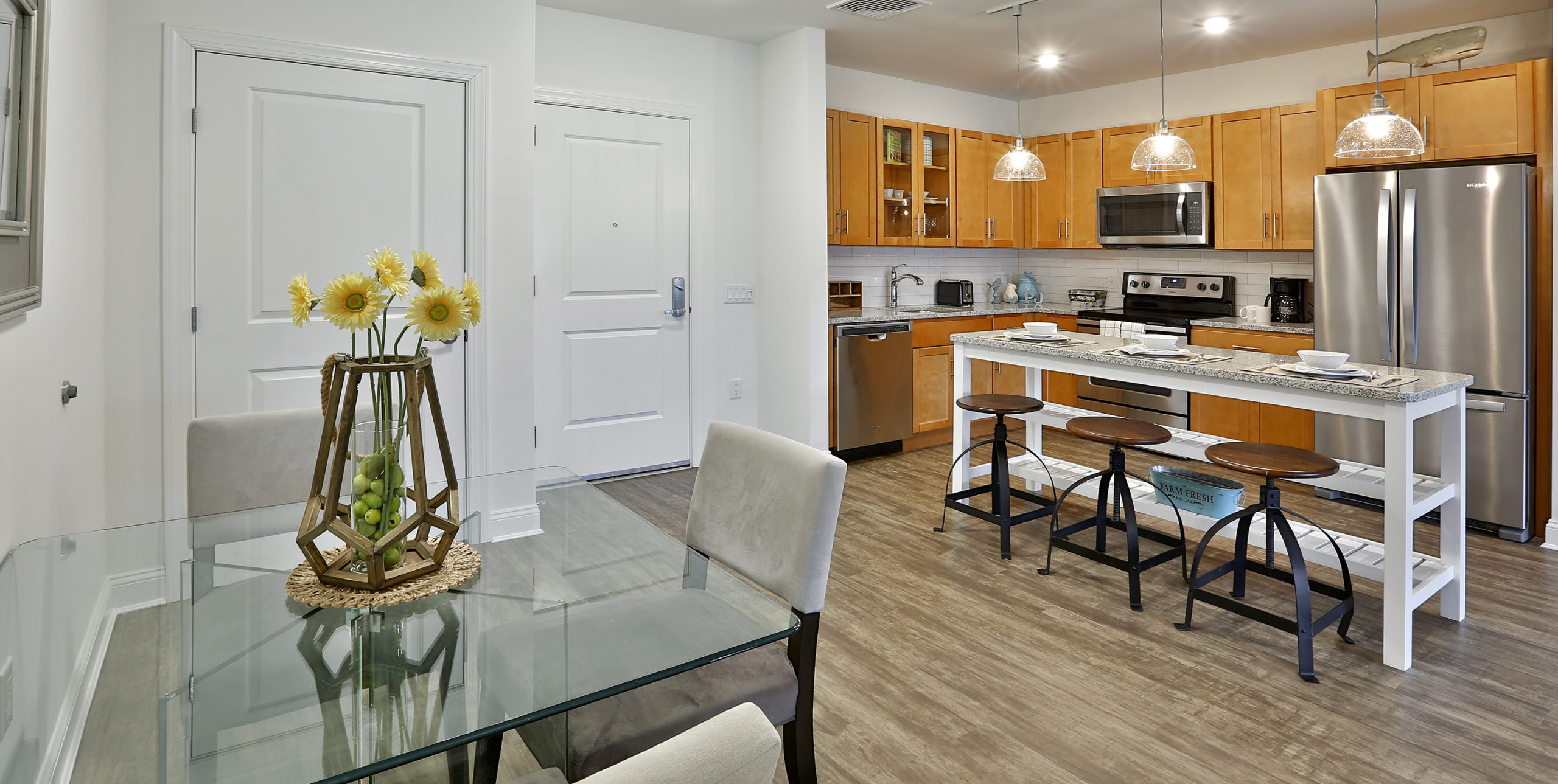 Kitchen of apartment at The Shipyard at Port Jeff Harbor with stainless steel appliances, an island with three stools, and a small side table with two chairs