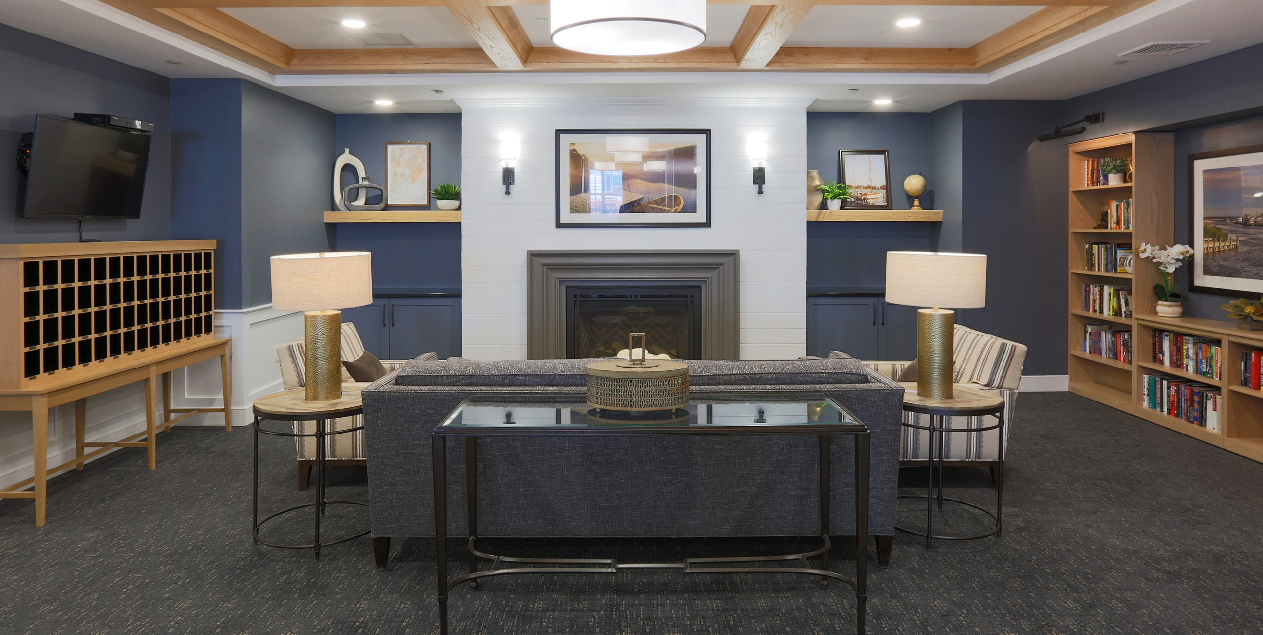 Cozy common area of three couches, two book shelves, a television and a fireplace at Brightview Senior Living in Sayville, NY