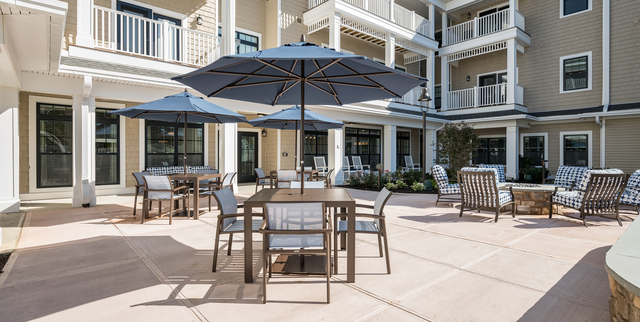 Outdoor patio with chairs, tables, and umbrellas and fireplaces at Brightview Senior Living Port Jeff