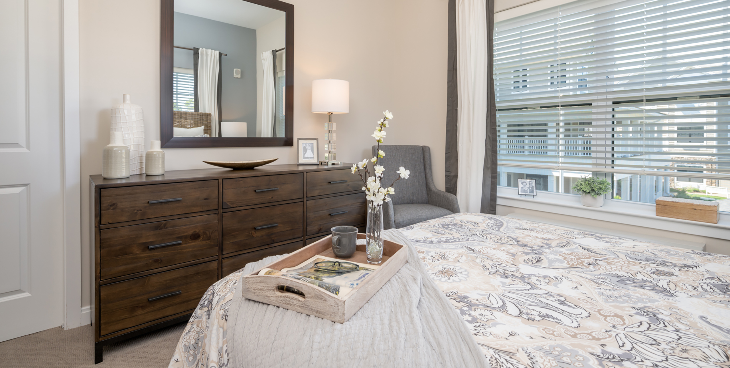 Queen sized bed in a bedroom in front of a dresser with a large mirror at Brightview Senior Living Port Jeff