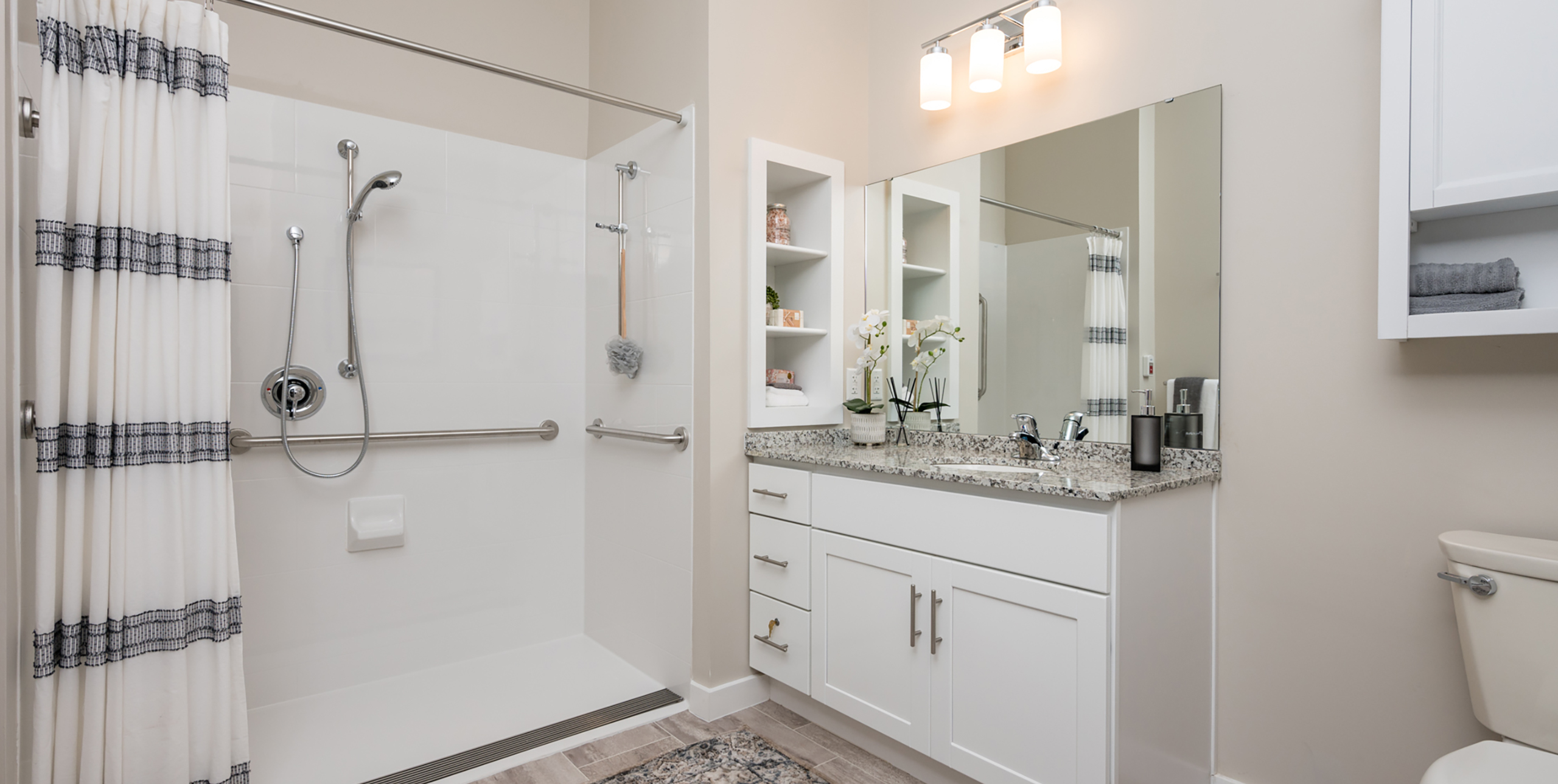 Handicap accessible shower in the bathroom with a sink and large mirror at Brightview Senior Living Port Jeff