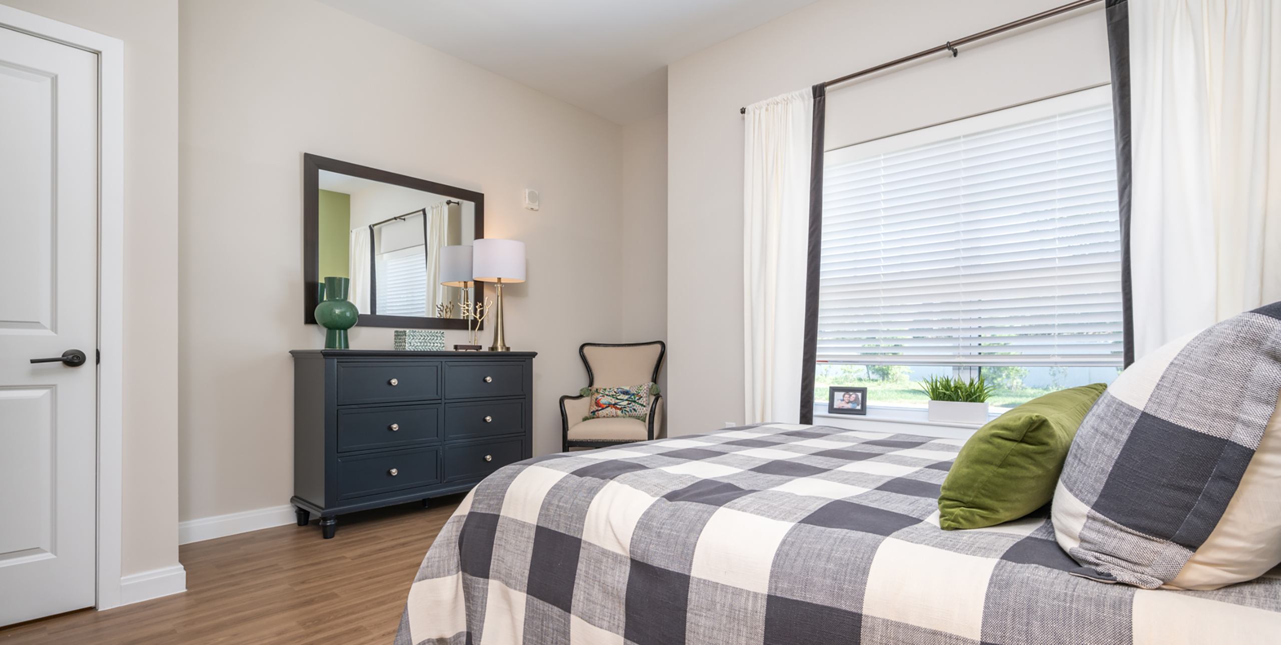 Bedroom with dresser, mirror and curtains at Brightview Senior Living Port Jeff